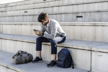 Mann sitzt auf einer Außentreppe und benutzt sein Smartphone - GIOF07251