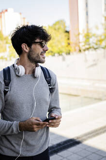 Smiling man holding smartphone in the city - GIOF07254