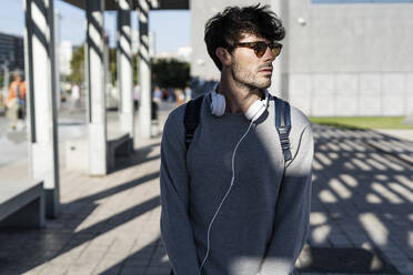 Man with sunglasses and headphones looking around in the city - GIOF07258