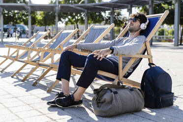 Man relaxing in deckchair on urban square listening to music - GIOF07264