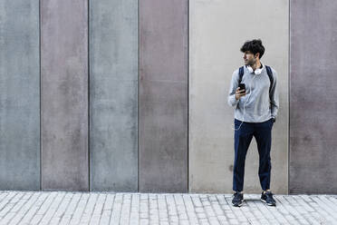 Man with cell phone and headphones standing in front of awall - GIOF07265