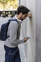 Man leaning against a wall checking cell phone - GIOF07269