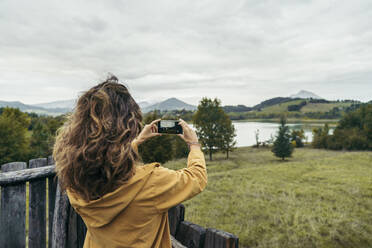 Junge Frau mit gelbem Mantel, die ein Foto mit ihrem Smartphone macht - MTBF00007