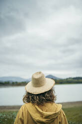 Rückansicht einer jungen Frau mit Strohhut, die auf einen See blickt - MTBF00012
