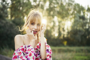 Portrait of blond young woman wearing summer dress with floral design at backlight - MTBF00028