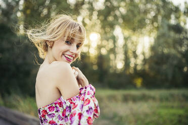 Portrait of happy young woman wearing summer dress with floral design in nature - MTBF00029