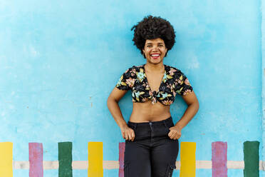 Lächelnde afro-amerikanische Frau vor einer blauen Wand, die in die Kamera schaut - ERRF01764