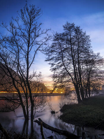 Deutschland, Bayern, Silhouetten von Bäumen gegen Fahrzeug Licht Spuren entlang des Ufers der Naab bei Sonnenuntergang Stretching, lizenzfreies Stockfoto