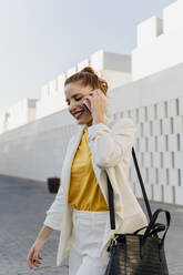 Geschäftsfrau in weißem Hosenanzug, die in der Stadt spazieren geht und telefoniert - ERRF01805