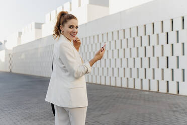 Businesswoman in white pant suit, using smartphone - ERRF01806
