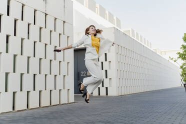 Happy businesswoman in white pant suit, jumping and dancing in the street - ERRF01814