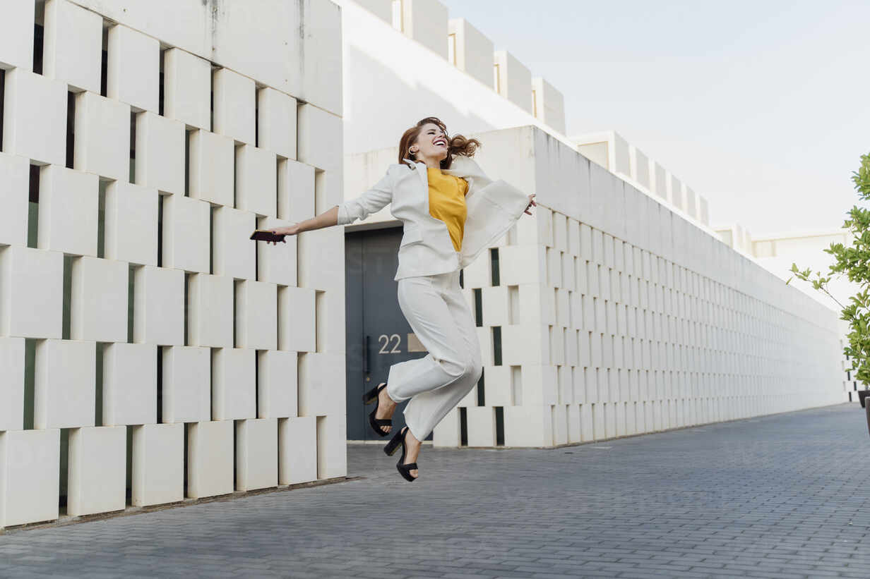 Happy businesswoman in white pant suit, jumping and dancing in the street  Stock Photo - Alamy
