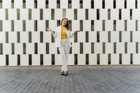 Geschäftsfrau in weißem Hosenanzug, vor einer Fassade stehend, gestikulierend, lizenzfreies Stockfoto