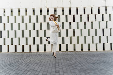 Happy businesswoman in white pant suit, jumping and dancing in the street - ERRF01817