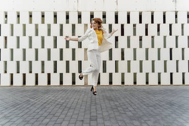 Happy businesswoman in white pant suit, jumping and dancing in the street - ERRF01818