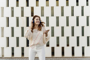 Geschäftsfrau, die auf der Straße geht und mit Kopfhörern Musik von ihrem Smartphone hört - ERRF01829