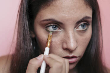 Nahaufnahme einer jungen brünetten Frau mit schönen blauen Augen, die Lidschatten mit einem Augenpinsel aufträgt - LOTF00077