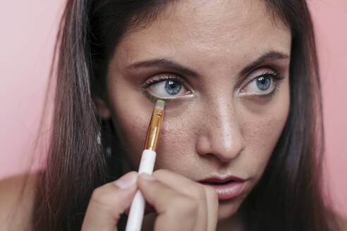 Close up of a young brunette woman with beautiful blue eyes applying eyeshadow with an eye brush - LOTF00077