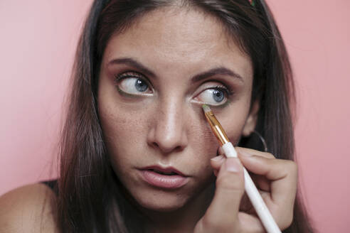 Close up of a young brunette woman with beautiful blue eyes applying eyeshadow with an eye brush - LOTF00078