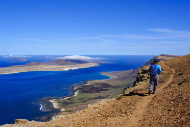 Spain, Canary Islands, Female backpacker hiking along edge of coastal cliff of La Graciosa island - SIEF09170