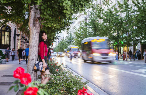 Junge Frau lehnt an einem Baum in der Stadt, lizenzfreies Stockfoto