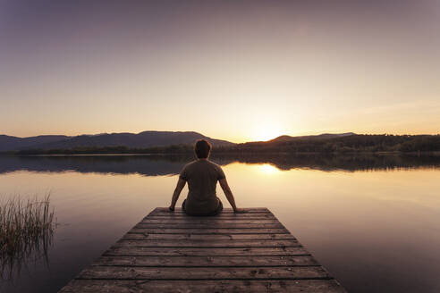 Silhouette of a man sitting on a wooden footbridge at sunset - MOSF00108