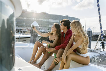 Three young friends enjoying a summer day on a sailboat, taking a selfie - MGOF04205