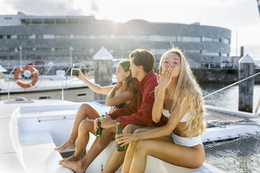 Three young friends enjoying a summer day on a sailboat, taking a selfie - MGOF04206