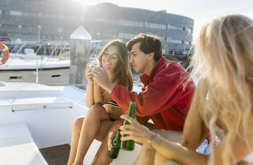 Drei junge Freunde, die einen Sommertag auf einem Segelboot genießen und ihr Smartphone benutzen - MGOF04207