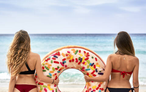 Two young women standing in front of the sea holding a big inflatable ring stock photo