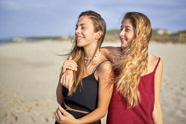 Two young women standing arm in arm on a beach - EPF00609