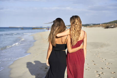 Zwei junge Frauen stehen Arm in Arm an einem Strand, lizenzfreies Stockfoto