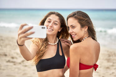 Zwei lächelnde junge Frauen machen ein Selfie am Strand - EPF00640