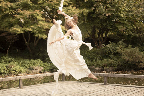 Ballerina in weißem Kleid und Sprung auf Holzsteg, lizenzfreies Stockfoto