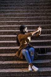 Weiblicher Tourist sitzt auf einer Treppe und macht ein Selfie im Freien - GIOF07283