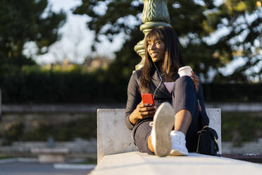 Lächelnde Geschäftsfrau, die im Freien sitzt und ihr Smartphone benutzt - GIOF07300