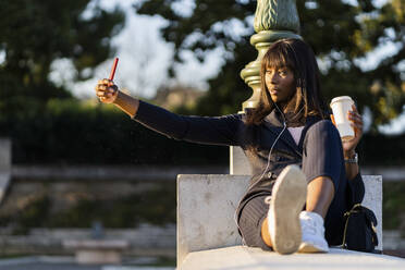 Lächelnde Geschäftsfrau sitzt im Freien und macht ein Selfie - GIOF07301