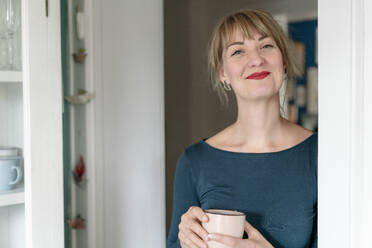 Porträt einer glücklichen Frau mit einer Tasse Kaffee zu Hause - KNSF06829