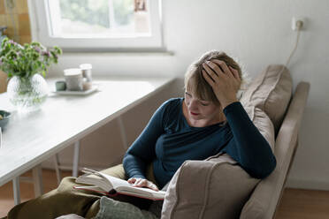 Woman sitting on couch reading a novel - KNSF06838