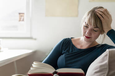 Portrait of woman reading a novel at home - KNSF06839