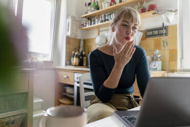Porträt einer jungen Frau, die in der Küche einen Laptop benutzt und sich einen Kuss zuwirft - KNSF06852
