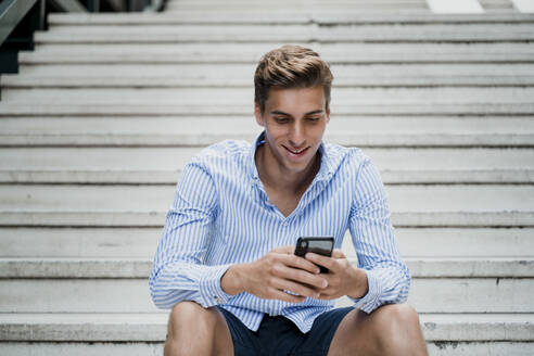 Young man sitting on stairs using his smartphone - JMHMF00023