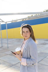 Porträt einer jungen Frau mit Coffee to go und Mobiltelefon - AFVF04080
