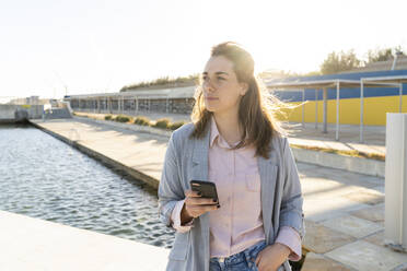 Portrait of young woman with mobile phone looking at distance - AFVF04086