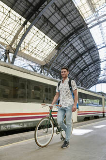 Mann schiebt Fahrrad durch einen Bahnhof - JNDF00129