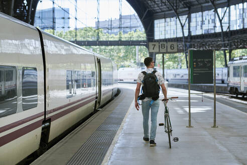 Mann schiebt Fahrrad durch einen Bahnhof - JNDF00130