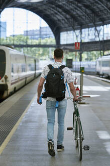Man pushing bicycle through a station - JNDF00131
