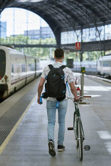 Mann schiebt Fahrrad durch einen Bahnhof - JNDF00131