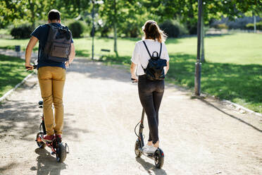 Back view of couple riding electric scooters in a city park - JSMF01316