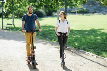 Couple riding electric scooters in a city park - JSMF01319